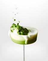 Coupe cocktail avec mousse blanche et éclaboussure de matcha vert sur fond blanc