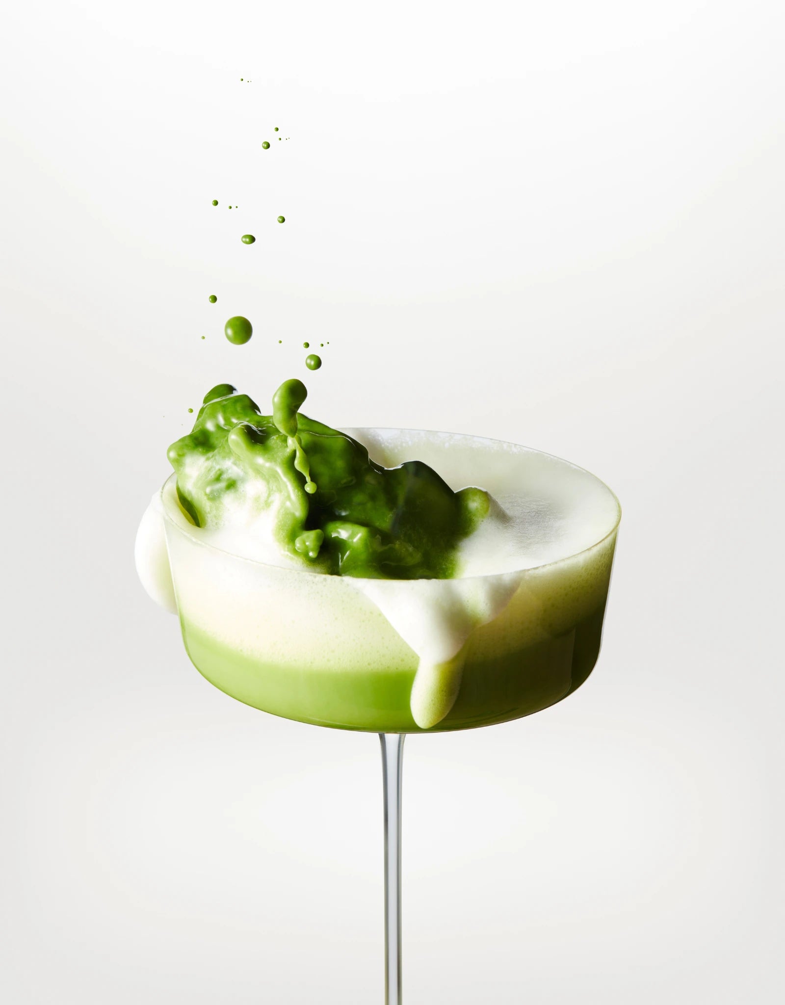 Coupe cocktail avec mousse blanche et éclaboussure de matcha vert sur fond blanc