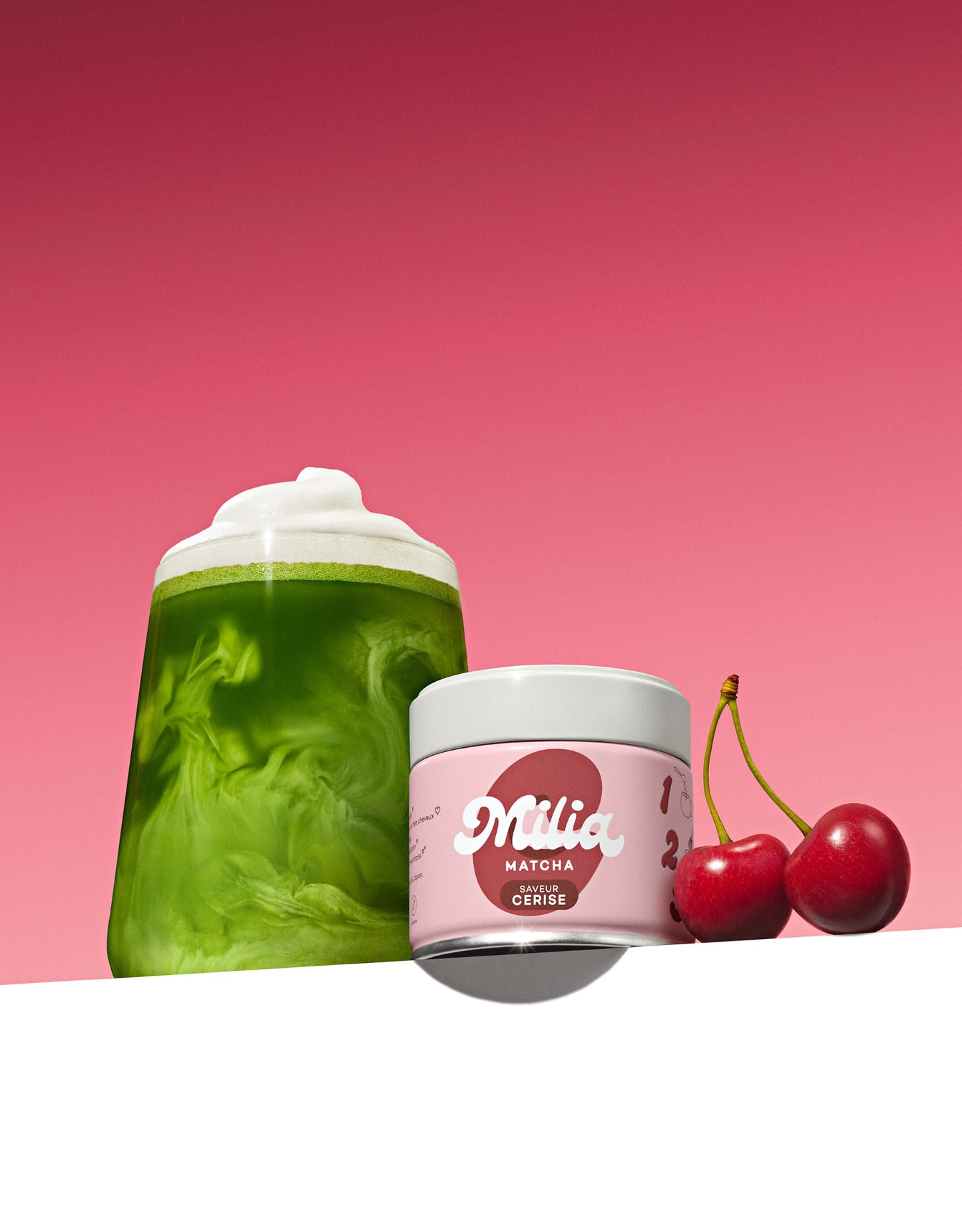 Verre de matcha premium aromatisé cerise avec canette et deux cerises sur fond rose fuchsia
