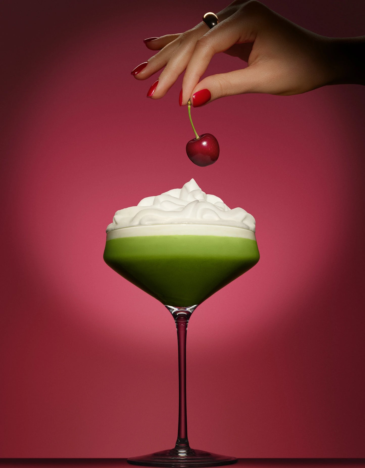 Cocktail matcha cerise Milia Matcha dans une coupe avec crème fouettée une main tenant une cerise au-dessus
