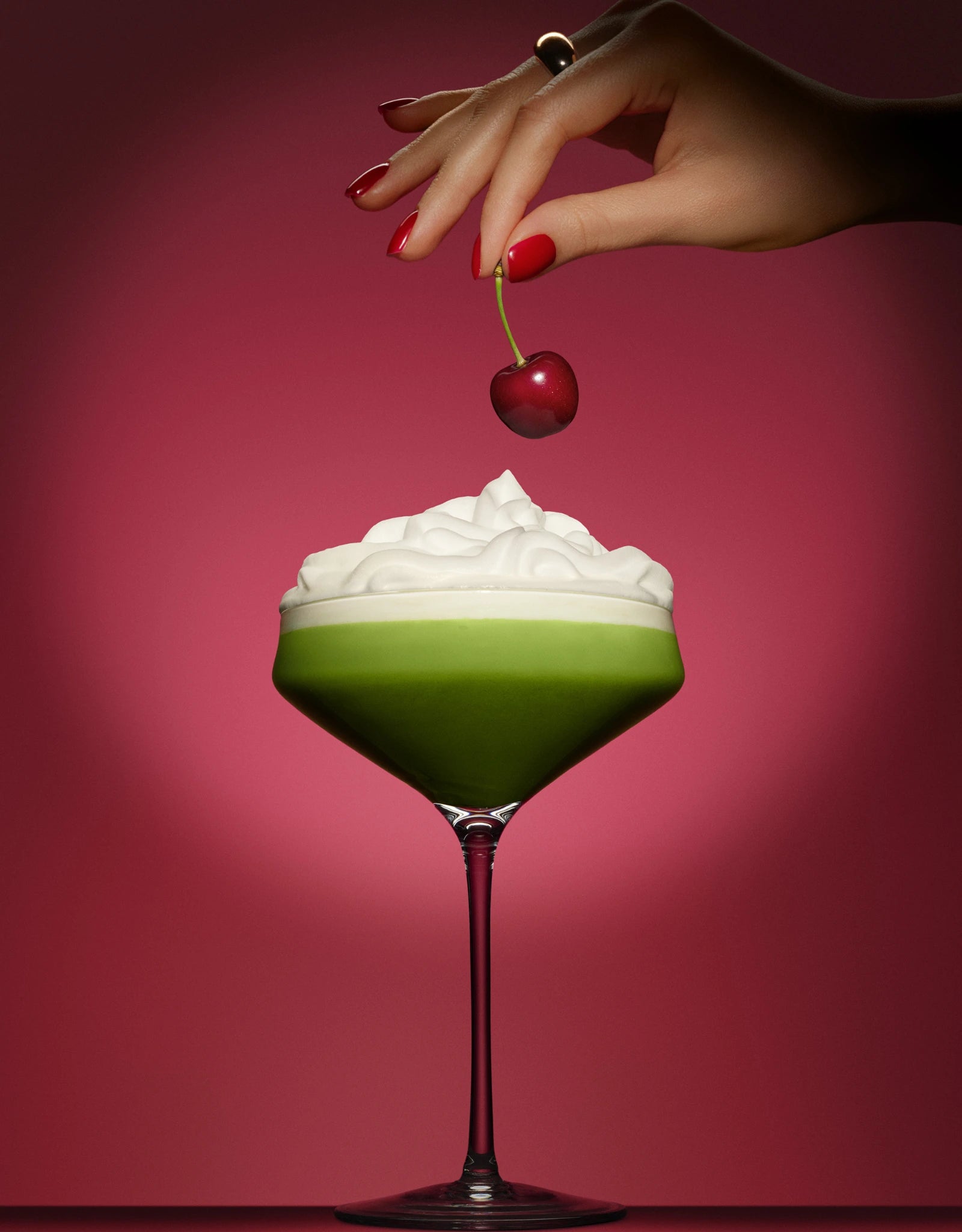 Cocktail matcha cerise Milia Matcha dans une coupe avec crème fouettée une main tenant une cerise au-dessus