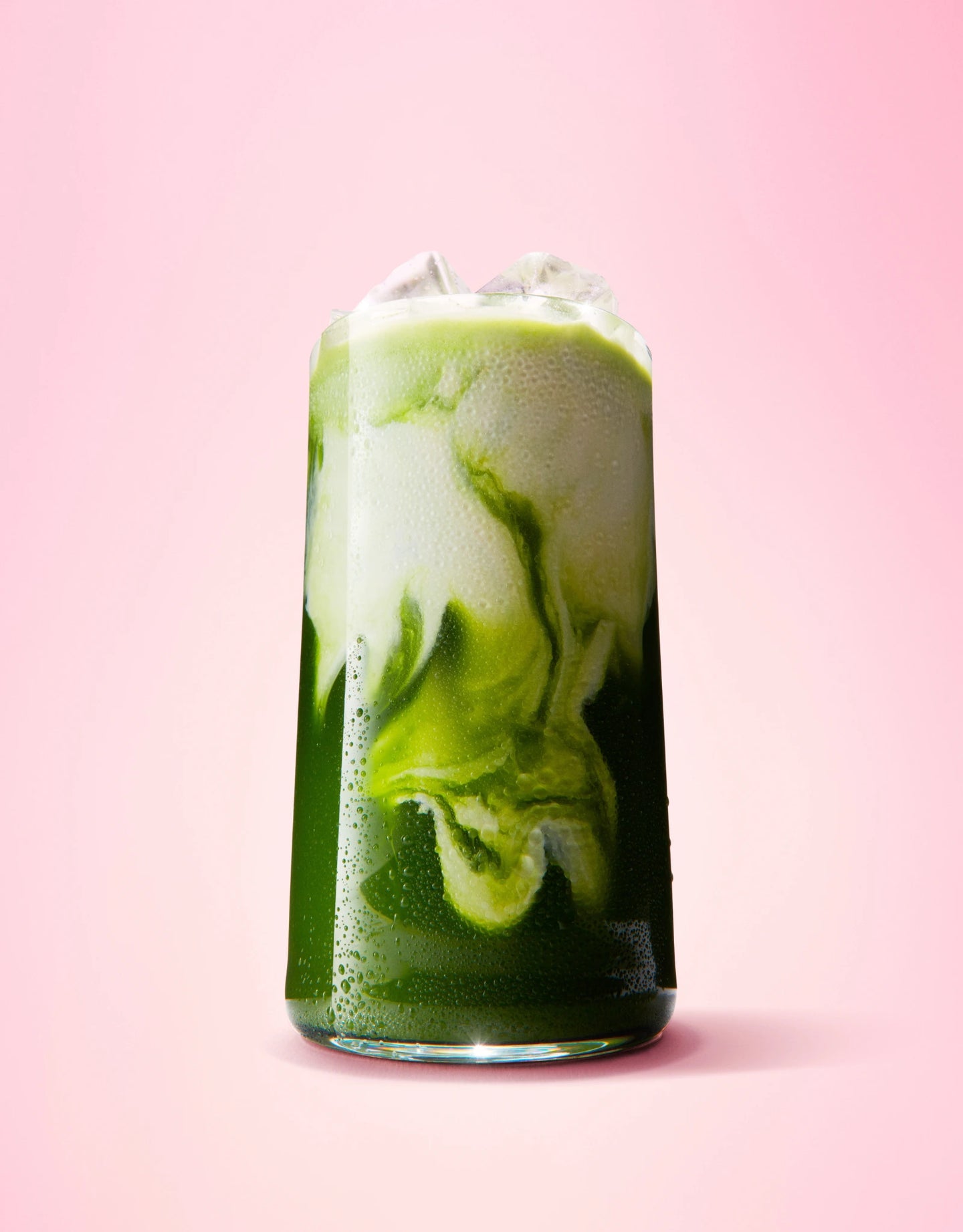 Verre matcha latte avec des glaçons sur fond rose 